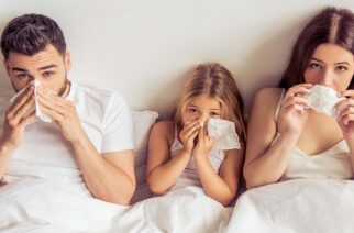 Beautiful young parents and their daughter are having common cold, wiping noses and looking at camera while lying on bed