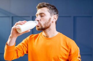 Conceptual portrait of a sports man in bright sweater drinking milk from the bottle on the blue background